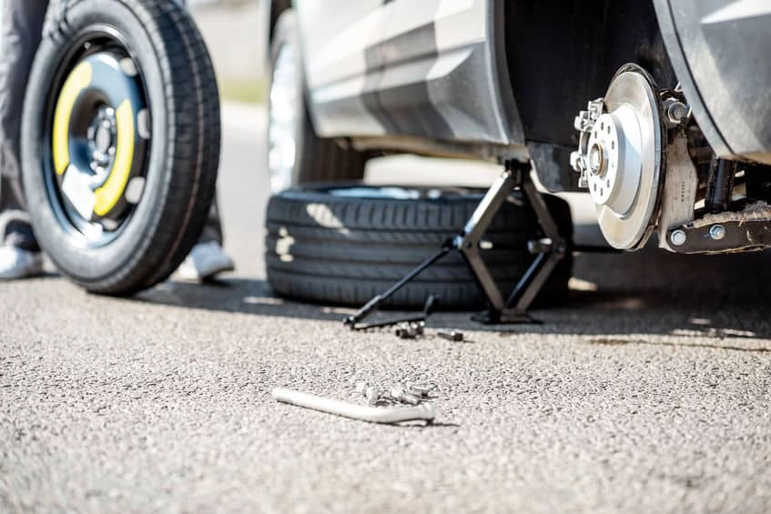 A person replacing a flat tire using a car jack and a lug wrench, ensuring safe and proper tire installation
